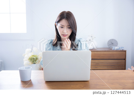 部屋でパソコンをみて考える悩む迷うかわいい女性　ちょっと真剣なネガティブイメージ　驚くビックリする 127444513