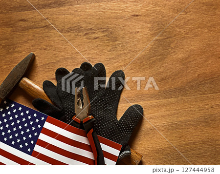 A textured wooden background with a pair of black work gloves, a hammer, and an American flag.  127444958