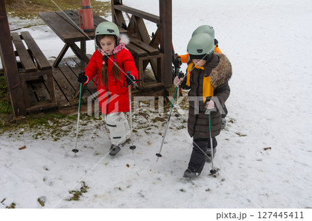 Winter fun unfolds as children navigate snowy terrain with skis and poles, cherishing the joy of outdoor adventure in a picturesque snowy landscape 127445411