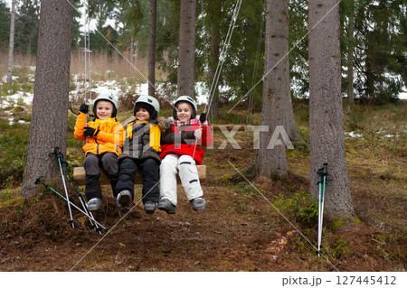 Children enjoying a swing in a winter forest while dressed warmly, surrounded by trees and snow, sharing smiles and laughter on a chilly afternoon Children enjoying a swing in a winter forest while dressed warmly, surrounded by trees and snow, sharing smiles and laughter on a chilly afternoon 127445412