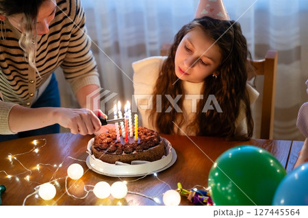 Delightful birthday celebration featuring a young girl, a beautifully decorated chocolate cake, and glowing candles during a cozy indoor gathering in the evening 127445564