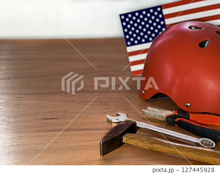 Red helmet, hammer, and wrench on a wooden surface with an American flag in the background. Red helmet, hammer, and wrench on a wooden surface with an American flag in the background. 127445928