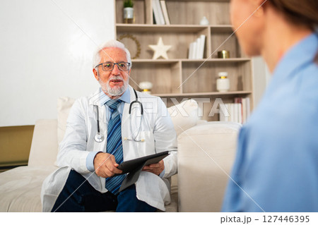 Senior man doctor examining young woman in doctor office clinic or at home. Girl patient and doctor have consultation in hospital room. Medicine healthcare medical checkup. Visit to doctor 127446395