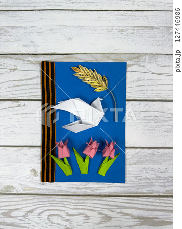Handmade Victory Day card on blue background with origami white doves pink paper carnation and a yellow black laurel wreath. Patriotic craft symbolizing peace memory and respect for war heroes 127446986