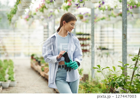 Florist woman is standing. Successful employee is in a bright greenhouse Florist woman is standing. Successful employee is in a bright greenhouse 127447003