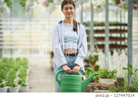 Beautiful florist woman working in garden center. Successful employee is in a bright greenhouse 127447014