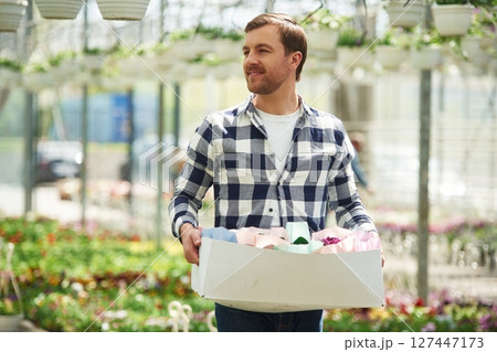 With paper box with stuff. Florist man working in garden center. Successful employee is in a bright greenhouse 127447173