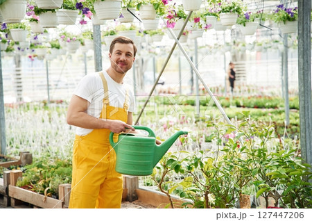 Green colored watering can. Florist man working in garden center. Successful employee is in a bright greenhouse 127447206