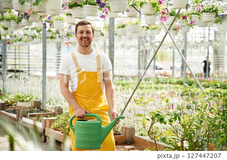 Green colored watering can. Florist man working in garden center. Successful employee is in a bright greenhouse 127447207