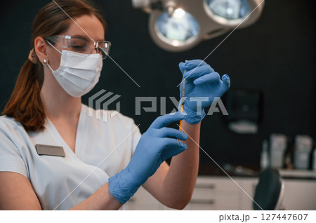 Doctor in blue glowes is standing and holding equipment. In the stomatological cabinet Doctor in blue glowes is standing and holding equipment. In the stomatological cabinet 127447607