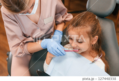 Woman teaching little girl how to brush teeth. In the stomatological cabinet Woman teaching little girl how to brush teeth. In the stomatological cabinet 127448338