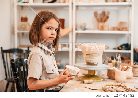 Little girl is indoors with ceramic pot in hands 127448482