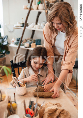 Creating the shape by using clay. Mother with little girl doing pottery at home 127448666