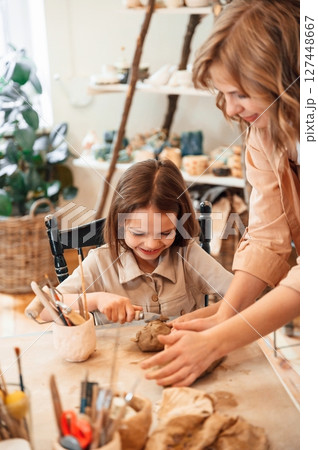 Creating the shape by using clay. Mother with little girl doing pottery at home Creating the shape by using clay. Mother with little girl doing pottery at home 127448667
