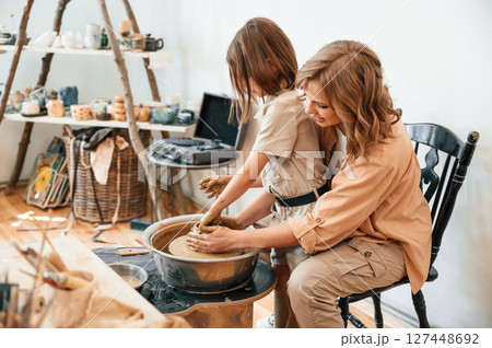 Pottery wheel. Mother with little girl making ceramic pot in the workshop 127448692