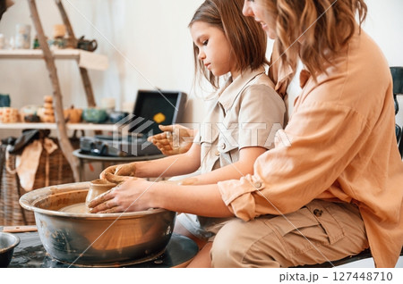 Sitting, creating the shape. Mother with little girl doing pottery at home 127448710