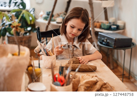 Working with clay. Little girl is learning how to do pottery in the workshop Working with clay. Little girl is learning how to do pottery in the workshop 127448758