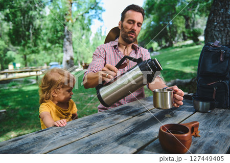 Father and Child Enjoying Outdoor Leisure at a Park Picnic Table Father and Child Enjoying Outdoor Leisure at a Park Picnic Table 127449405