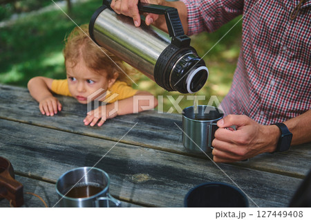 Father Pouring Drink from Thermos While Daughter Watches Outdoors Father Pouring Drink from Thermos While Daughter Watches Outdoors 127449408