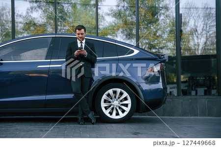 Holding smartphone. Businessman is standing near his car outdoors 127449668