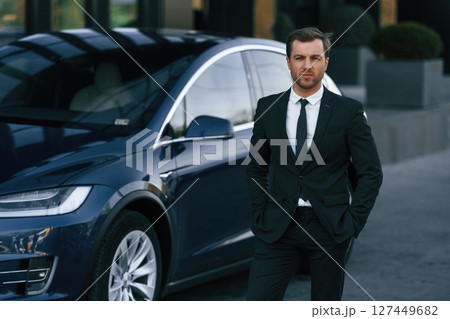 Standing, in black suit. Businessman is near his car outdoors 127449682