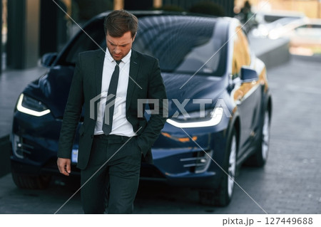 In suit and tie. Businessman is standing near his car outdoors In suit and tie. Businessman is standing near his car outdoors 127449688
