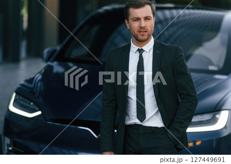 In suit and tie. Businessman is standing near his car outdoors In suit and tie. Businessman is standing near his car outdoors 127449691