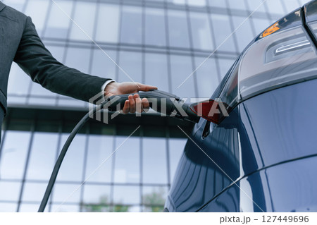 Close up view, putting charger into the socket. Businessman is standing near his electric car outdoors 127449696