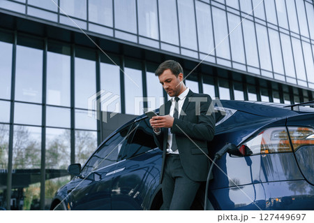 Using smartphone. Businessman is standing near his car outdoors Using smartphone. Businessman is standing near his car outdoors 127449697