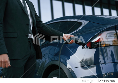 Close up view, putting charger into the socket. Businessman is standing near his electric car outdoors 127449700