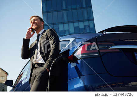 Business call, talking by phone. Man is standing near his electric car outdoors 127449726