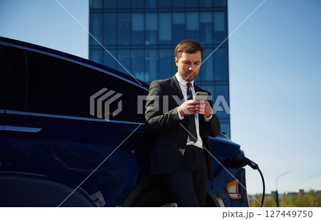 Waiting for a charge. Businessman is standing near his electric car outdoors 127449750