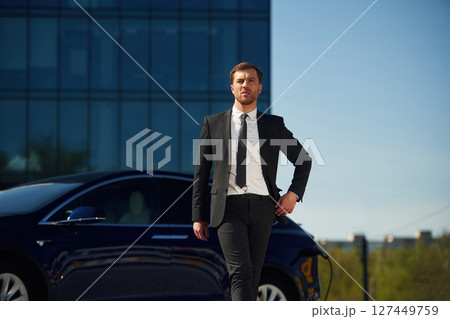 Serious facial expression. Businessman is standing near his electric car outdoors 127449759