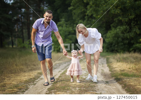 Husband, wife and their little daughter for a walk in the park. Happy dad and mom are walking through the woods with their one-year-old daughter. Husband, wife and their little daughter for a walk in the park. Happy dad and mom are walking through the woods with their one-year-old daughter. 127450015