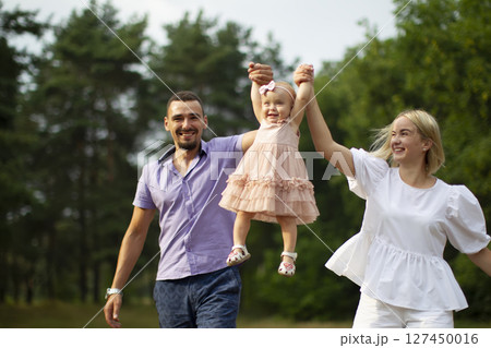 Husband, wife and their little daughter for a walk in the park. Happy dad and mom throws up their little laughing one-year-old daughter. 127450016
