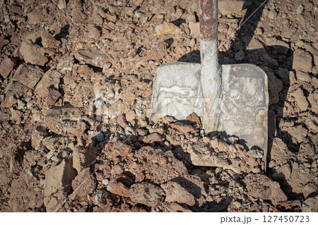 Groundbreaking work with a shovel in dry earth at a construction site during daytime Groundbreaking work with a shovel in dry earth at a construction site during daytime 127450723