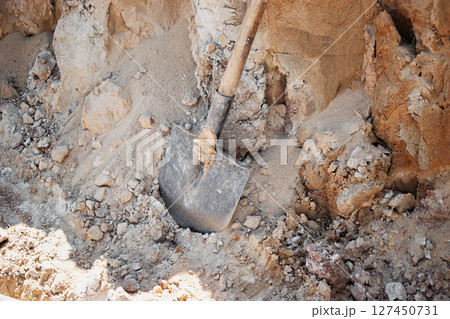 Shovel resting in a pile of dirt at a construction site in midday sun near a developing area 127450731