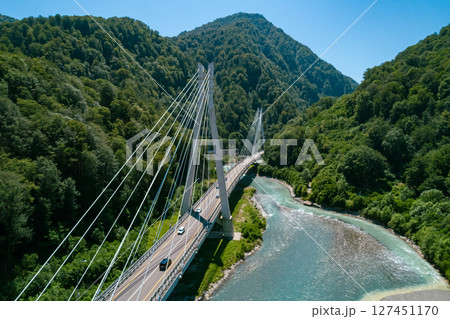 A suspension bridge stretches across a flowing river, surrounded by lush green mountains A suspension bridge stretches across a flowing river, surrounded by lush green mountains 127451170