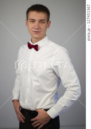 Classic portrait of a young man on a gray background. A guy of about twenty in a white shirt and bow tie. Classic portrait of a young man on a gray background. A guy of about twenty in a white shirt and bow tie. 127451367