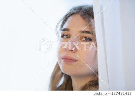Close-up of the face of a young girl peeping out of the curtains. Close-up of the face of a young girl peeping out of the curtains. 127451412