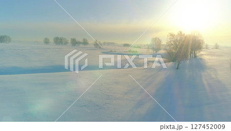 Aerial view of cold winter landscape arctic field, trees covered with frost snow, ice river and sun rays over horizon. Extreme low temperature weather. 127452009
