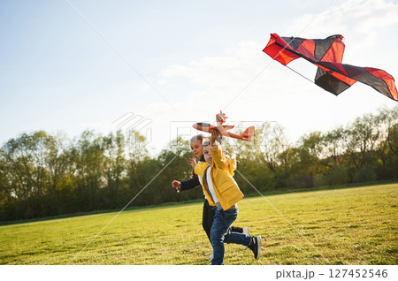 Two kids are playing with kite on the summer field Two kids are playing with kite on the summer field 127452546