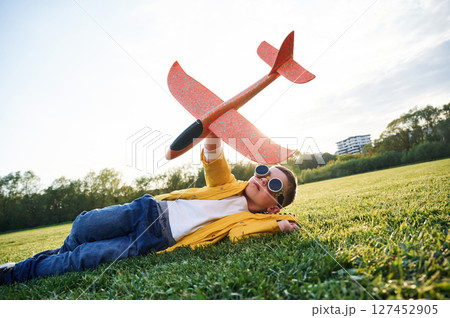 Lying down on ground. Little boy is playing with toy plane on the summer field 127452905