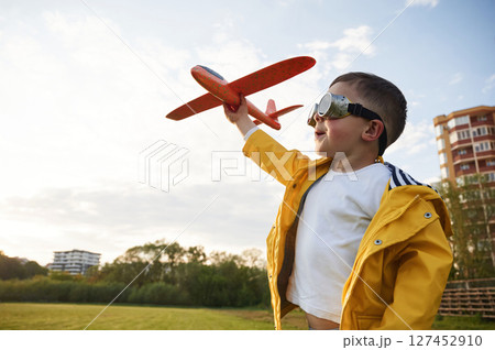 Red colored toy plane. Little boy is playing on the summer field 127452910