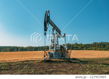 A large oil pump jack operates in an open field, extracting crude oil A large oil pump jack operates in an open field, extracting crude oil 127453905
