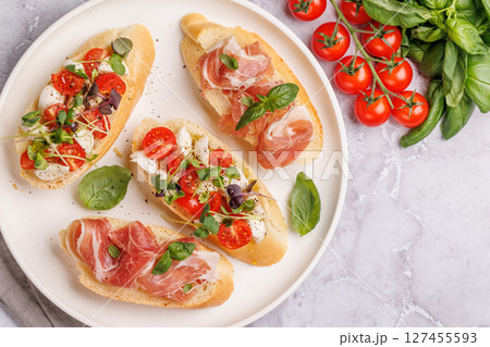 Tasty antipasto toasts featuring classic caprese with mozzarella and tomatoes, and savory prosciutto with herbs Tasty antipasto toasts featuring classic caprese with mozzarella and tomatoes, and savory prosciutto with herbs 127455593