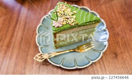 close up of a slice of green pistachio cream cake with layers on a floral plate with copy space on the wooden table  127456646