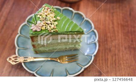 close up of a slice of green pistachio cream cake with layers on a floral plate with copy space on the wooden table  127456648