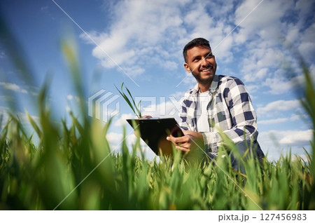 Quality check. Sitting with notepad and wheat. Handsome Indian man is on the agricultural field 127456983