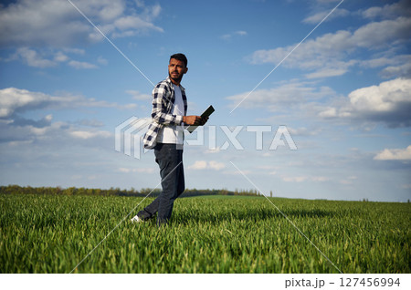 Standing and holding notepad. Handsome Indian man is on the agricultural field 127456994